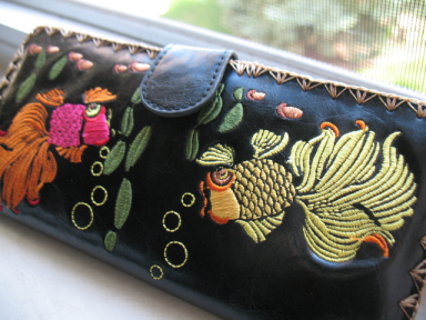 Front view of a black faux-leather wallet with colorful embroidered fish.