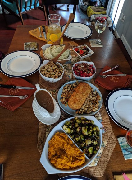 A slightly skewed top-down view of a kitchen table loaded with food and plates.