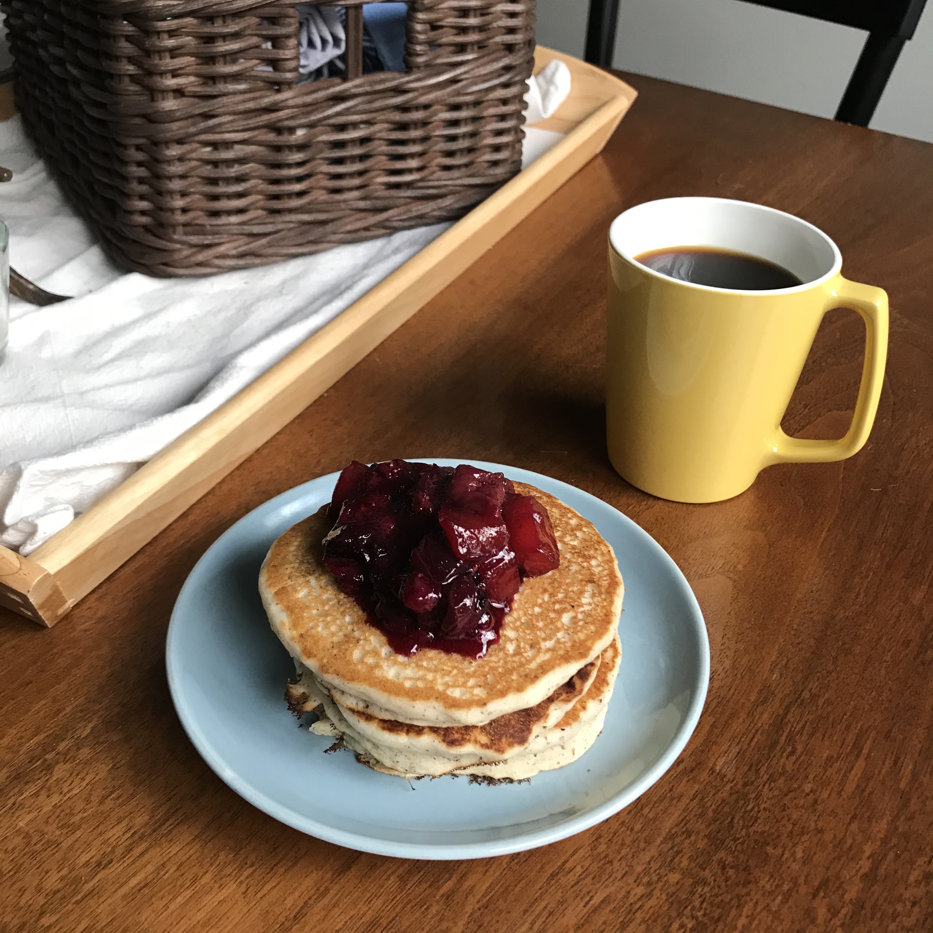 A small blue plate with a stack of pancakes, topped with a deep red fruit compote.
